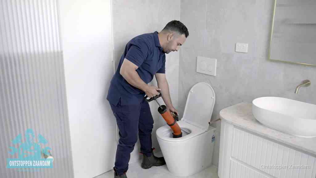 Een monteur buigt over een wandcloset en duwt met de hand een persluchtontstopper in de toiletpot om de verstopping handmatig los te maken in Zaandam