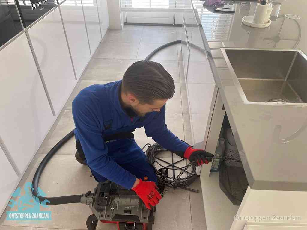 Een monteur ontstopt de keukenafvoer onder de spoelbak met een elektrische veermachine in Zaandam