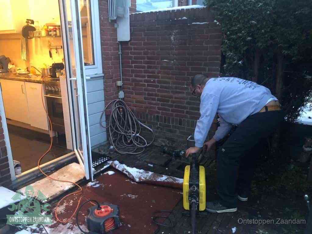 Een monteur werkt buiten bij een open riool-/grondput met een elektrische ontstoppingsmachine om een verborgen afvoerprobleem op te sporen in Zaandam
