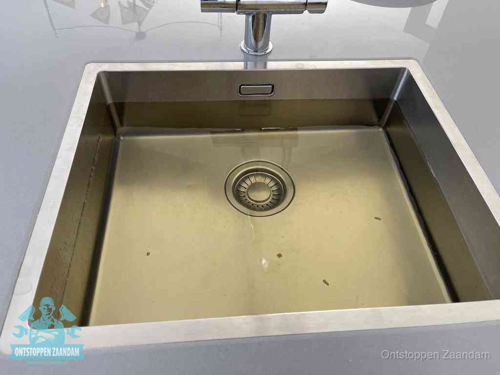 Stilstaand water in een rvs spoelbak dat niet wegloopt, een duidelijk signaal van een gootsteenverstopping in Zaandam