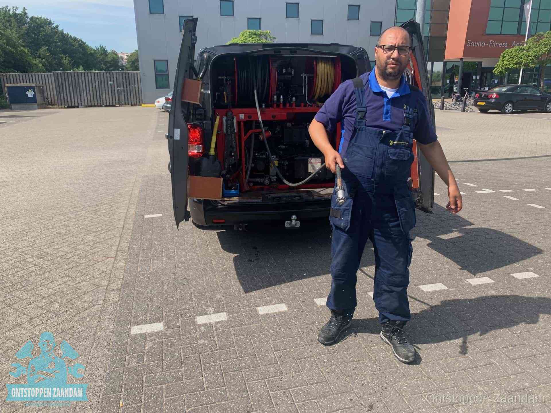 Een monteur bij zijn bestelbus met een hogedruk- en rioolreinigingsunit, klaar om de oorzaak van terugkerende wc-verstoppingen aan te pakken in Zaandam