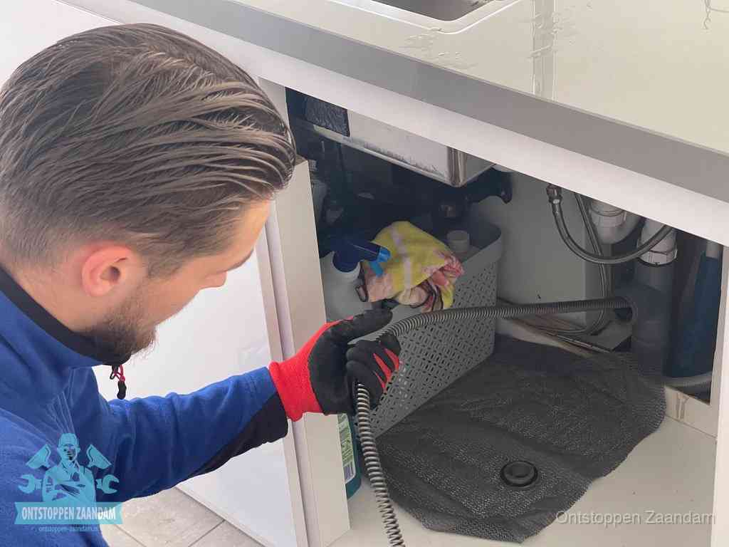Een monteur voert een flexibele ontstoppingsveer in de afvoer om een verstopping voorbij de bocht van het toilet te bereiken in Zaandam