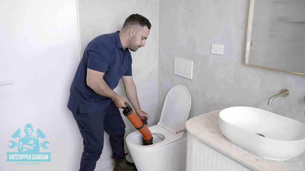 Een man gebruikt een handmatige luchtdruk-ontstopper in een modern betegeld toilet om zelf de wc te ontstoppen in Zaandam